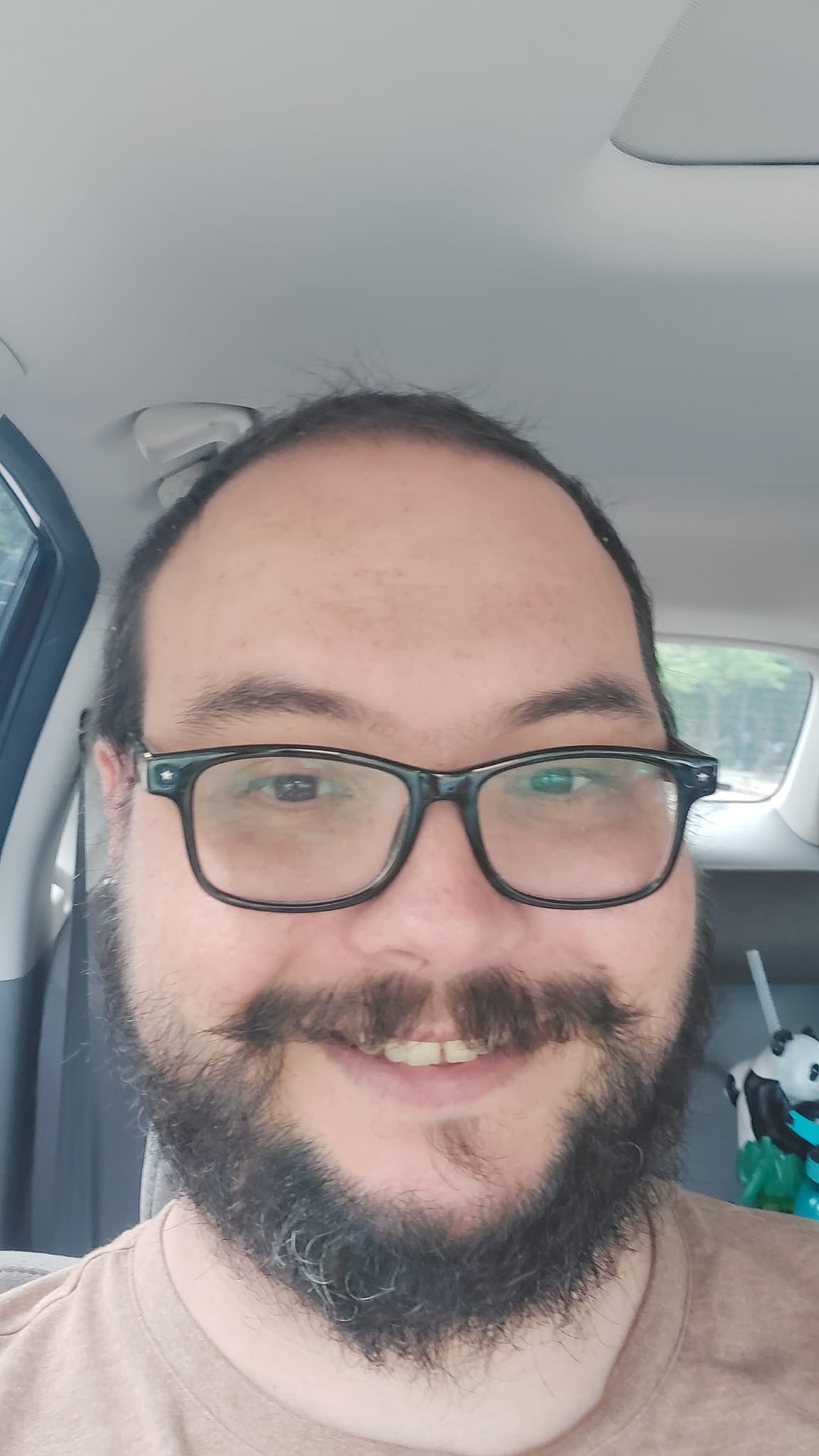 A man short hair and bushy facial hair sits happily in a car